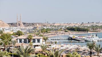 A coastal cityscape with a prominent mosque, a marina with boats, and a beach area with umbrellas.