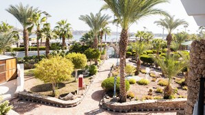 A landscaped garden with palm trees and shrubs, a paved walkway, and a view of the sea. - Turquoise Beach Hotel (Sharm El Sheikh)