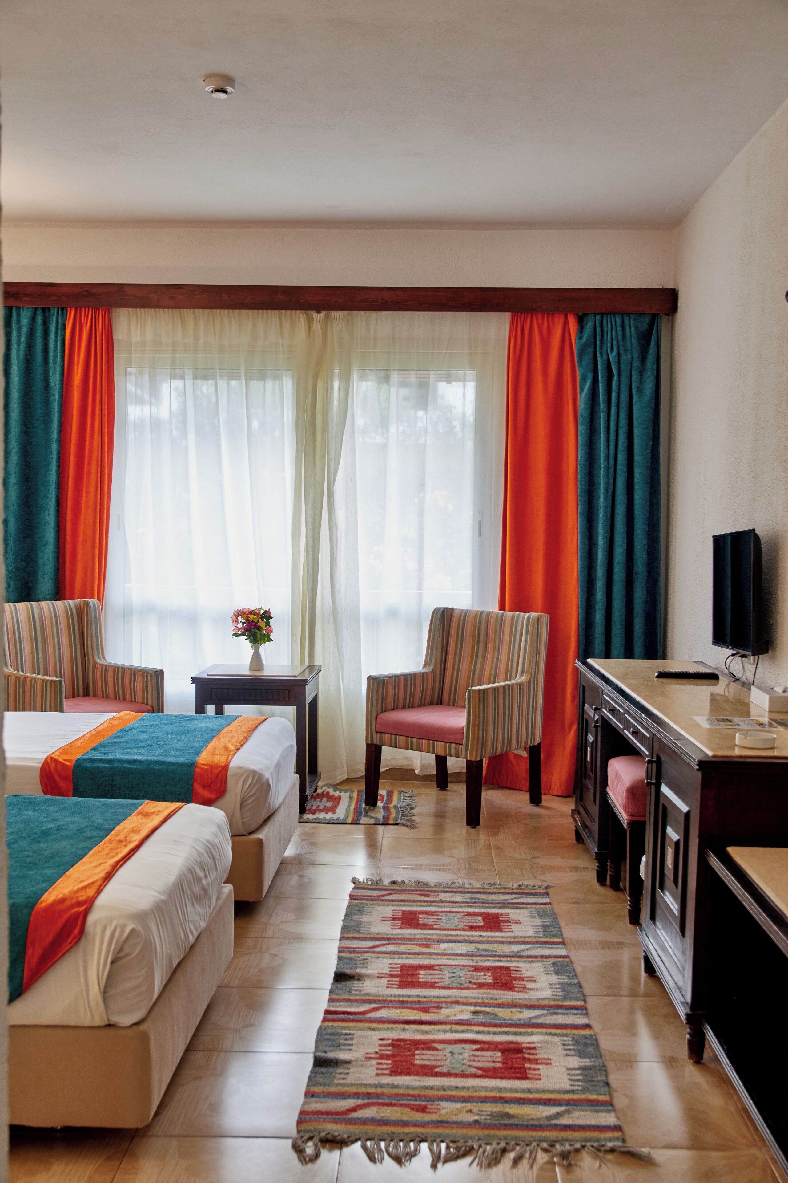 A hotel room with two beds, a desk, a chair, a TV, and a window with curtains.
