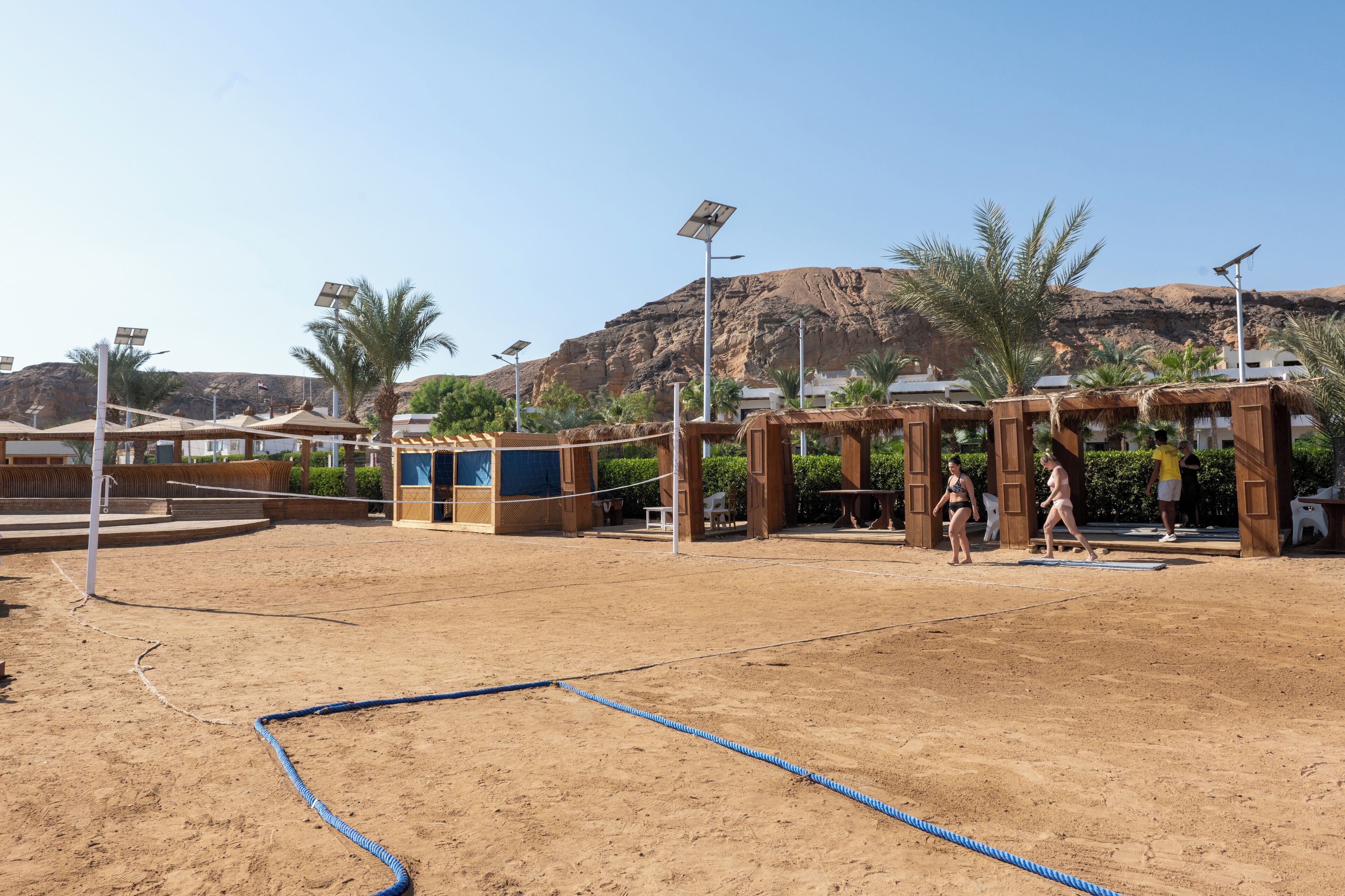 Een strandvolleybalveld met net, palmbomen en een bergachtige achtergrond.