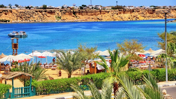 A beach with umbrellas, lounge chairs, and a lifeguard tower. - Turquoise Beach Hotel (Sharm El Sheikh)