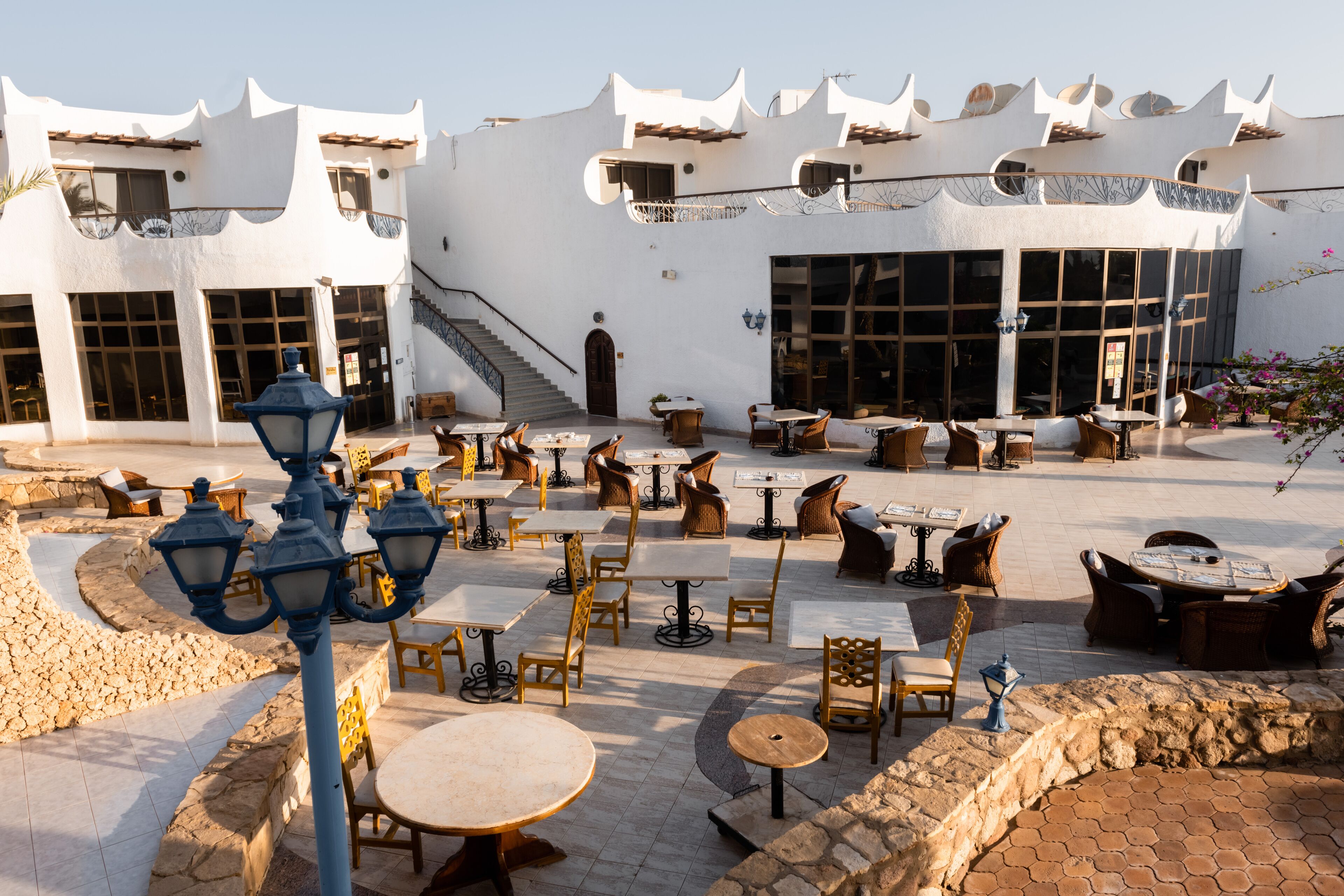An outdoor cafe area with tables and chairs, a staircase, and a building with a unique architectural design.