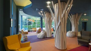 Un vestíbulo moderno con un sillón amarillo, coloridos pufs y una estructura de madera original.