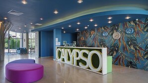 Un área de recepción con un letrero 'CALYPSO', un ventanal grande y una pared con un estampado de hojas de colores.