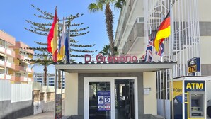 La entrada al hotel D. Gregorio, con un cajero automático y carteles informativos sobre COVID-19.