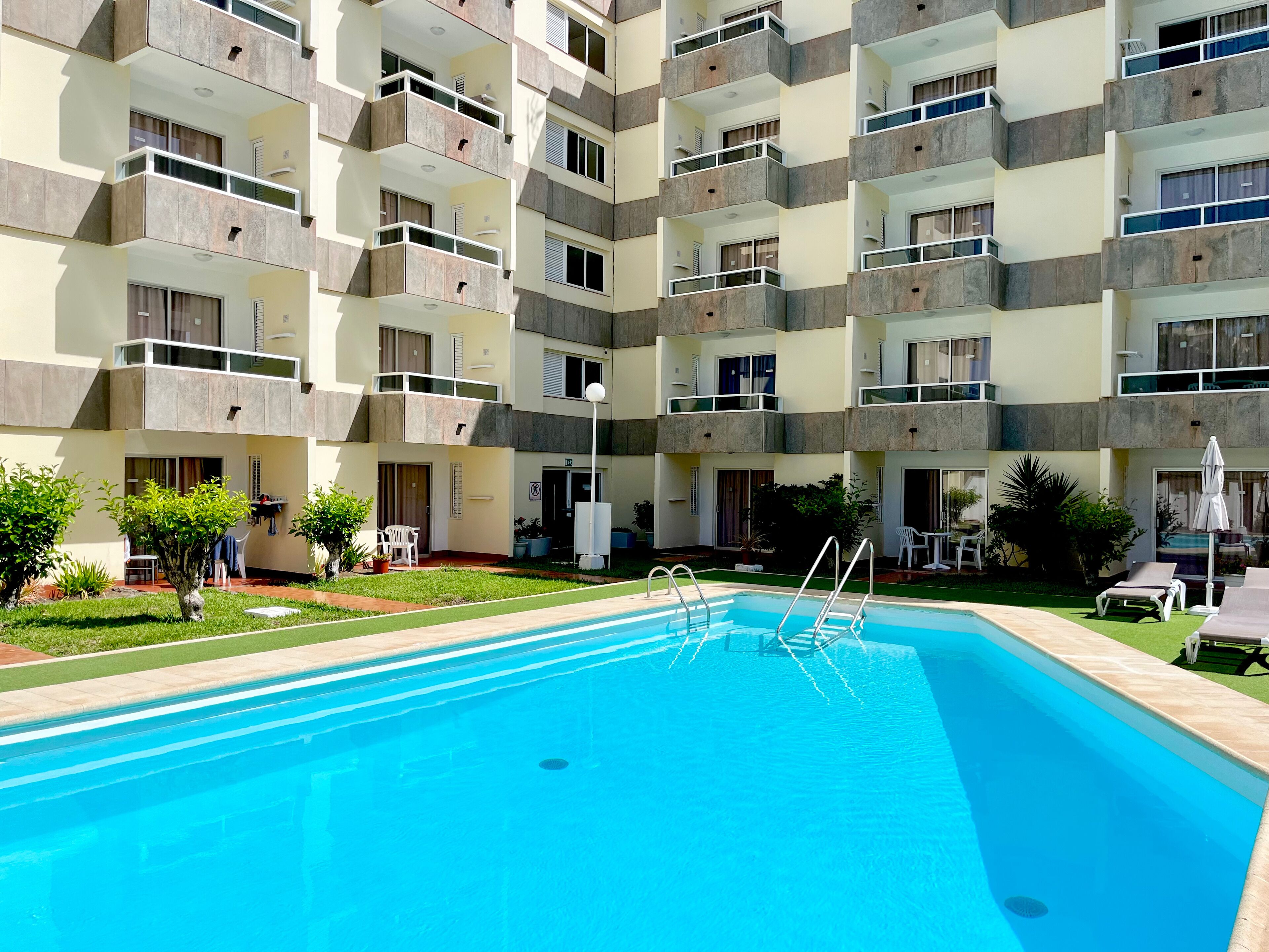A multi-story residential building with balconies, a swimming pool, and outdoor seating areas.