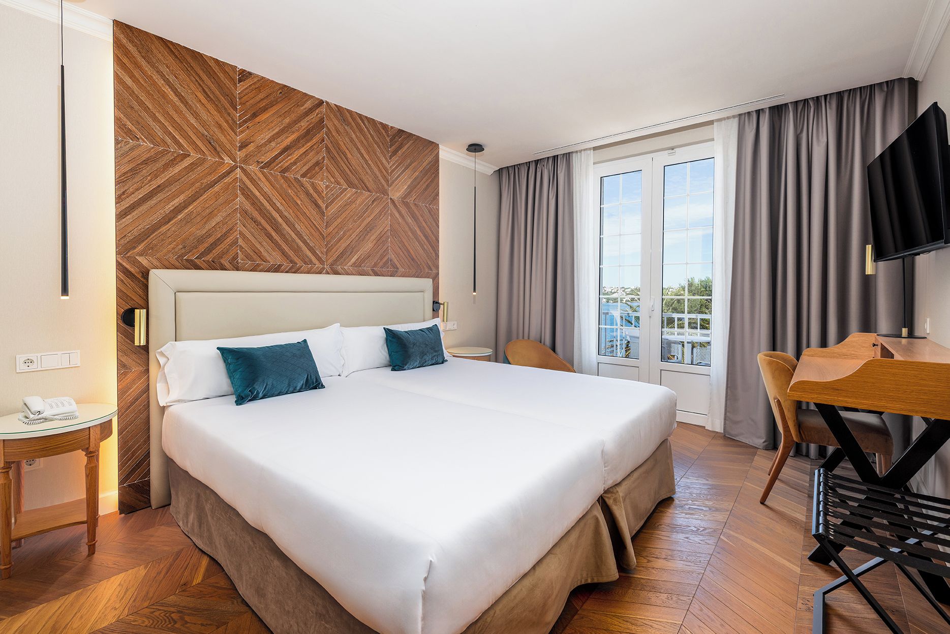 A hotel room with a large bed, a desk with a chair, a television, and a view of the outdoors.