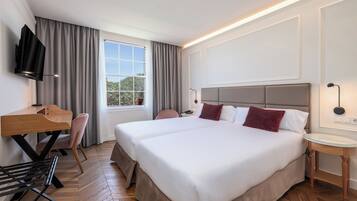 A hotel room with a large bed, a desk, a chair, a TV, and a window with curtains.
