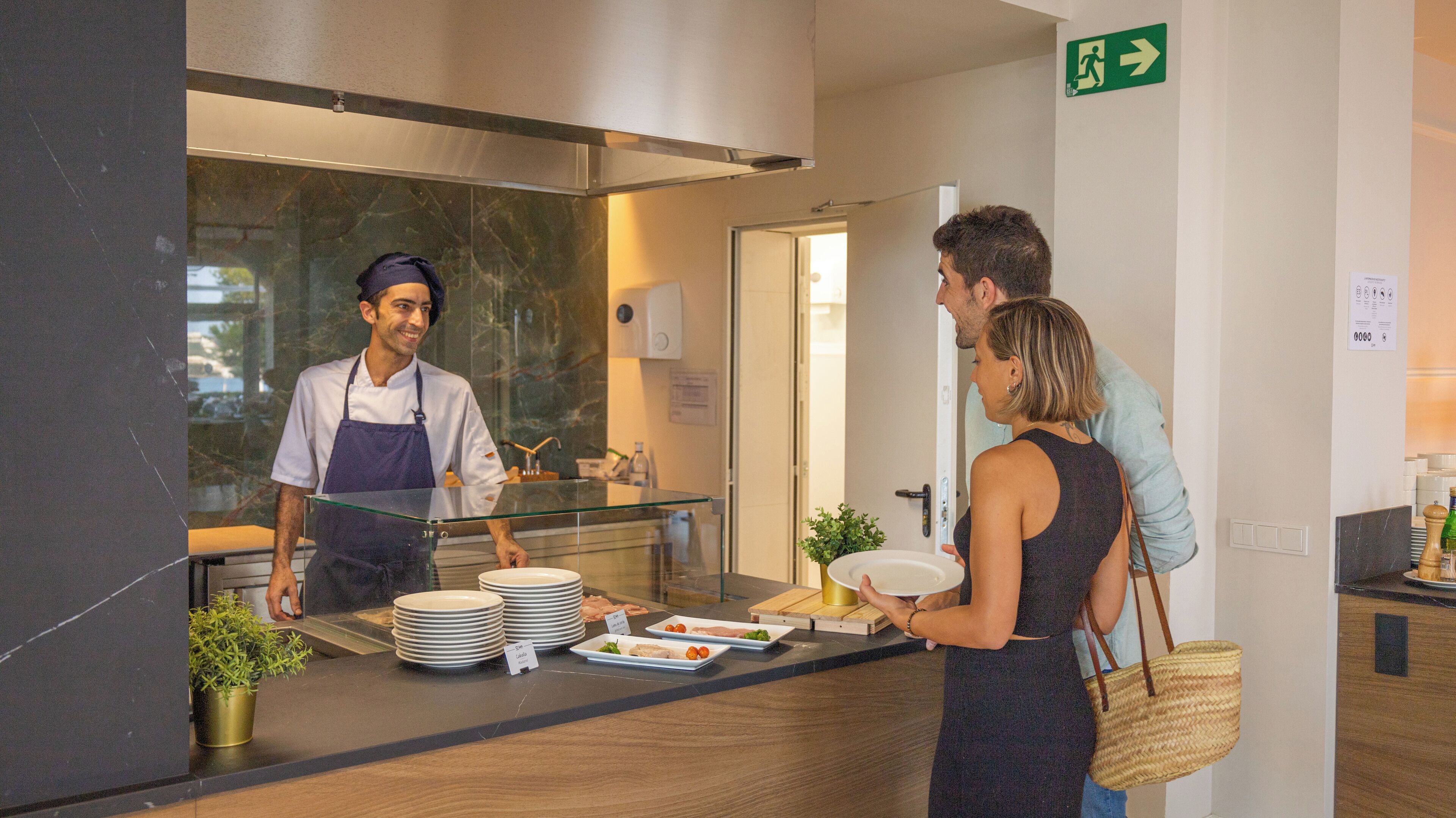 Zona de recepción de un hotel con mostrador, un miembro del personal y un huésped.