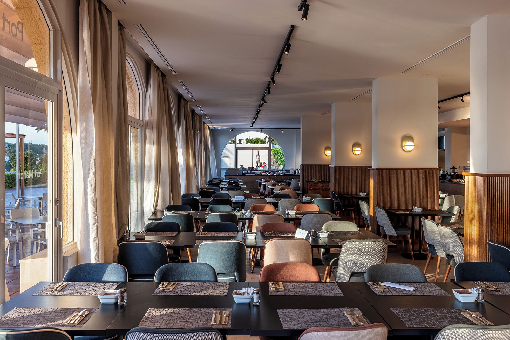 Ein Restaurant mit mehreren Tischen, Stühlen, einer langen Theke und Blick durch ein großes Fenster.