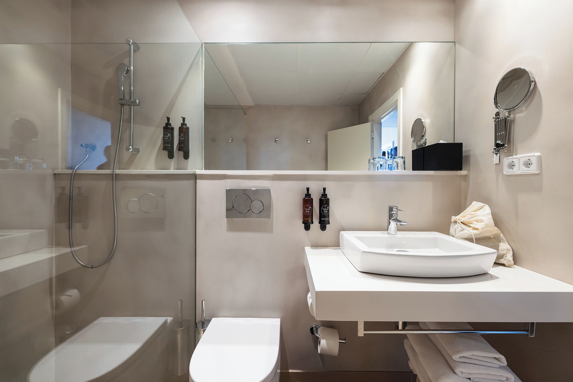 Ein modernes Badezimmer mit einer gläsernen Duschkabine, einem weißen Waschbecken und einem Spiegel darüber.