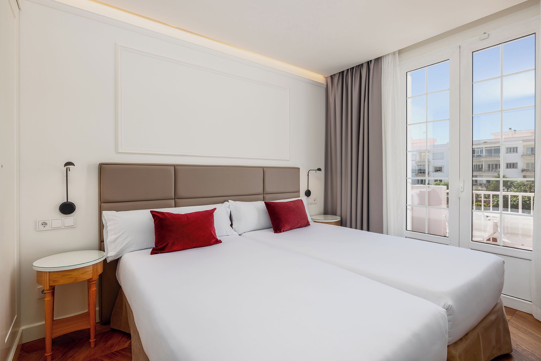 A hotel room with a double bed, two bedside tables, a wall-mounted lamp, and a large window with curtains.