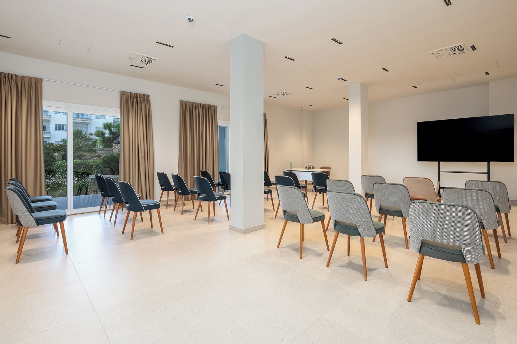 A conference room with a large flat-screen TV, multiple chairs, a table, and a view through large windows.