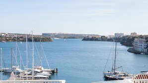 Un port de plaisance où sont amarrés de nombreux voiliers, une ville côtière en arrière-plan et un ciel dégagé.