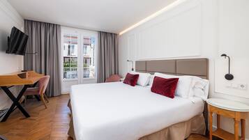 Habitación de hotel con una cama grande, un escritorio, una silla, un televisor y una ventana con cortinas.