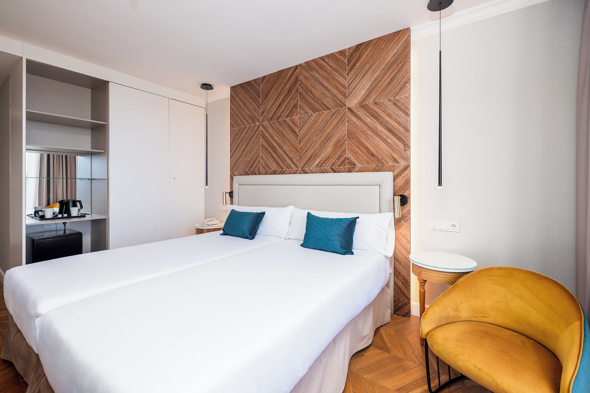 A hotel room with a large bed, a bedside table, a chair, and a wardrobe.