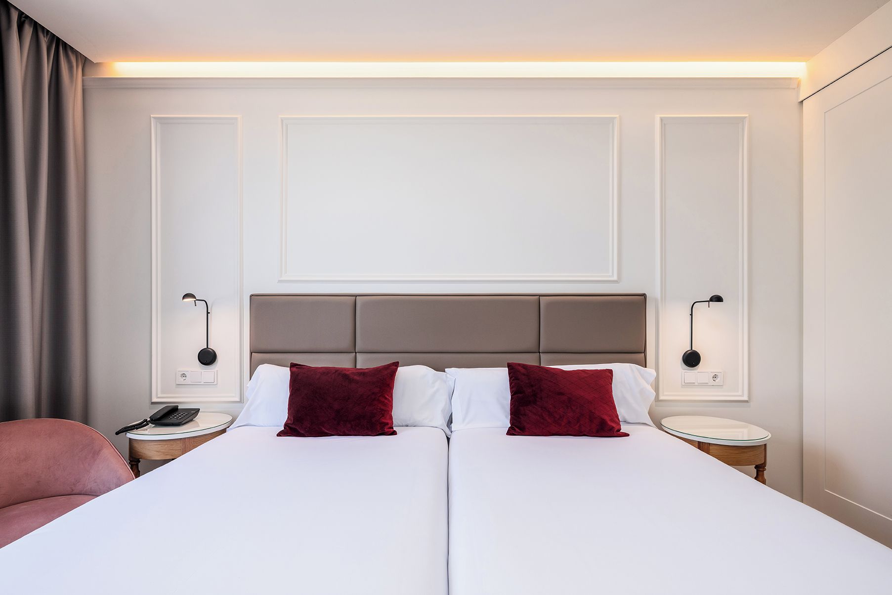 A double bed with a headboard, two bedside tables with lamps, a telephone, and a red chair.