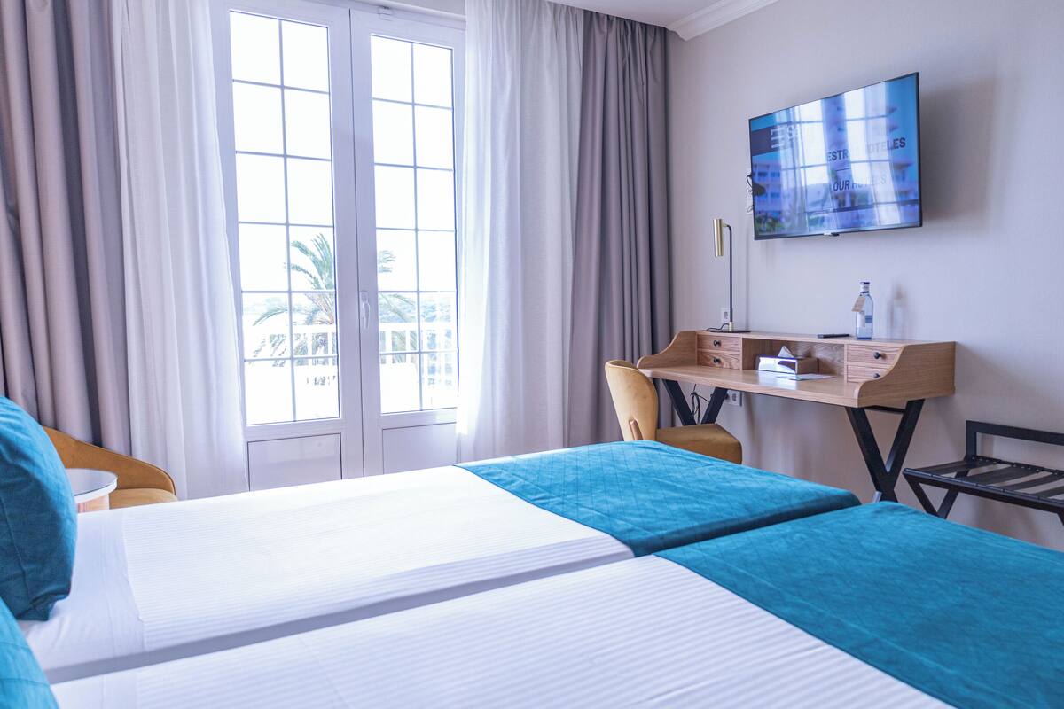 A hotel room with two beds, a desk, a chair, and a TV on the wall.