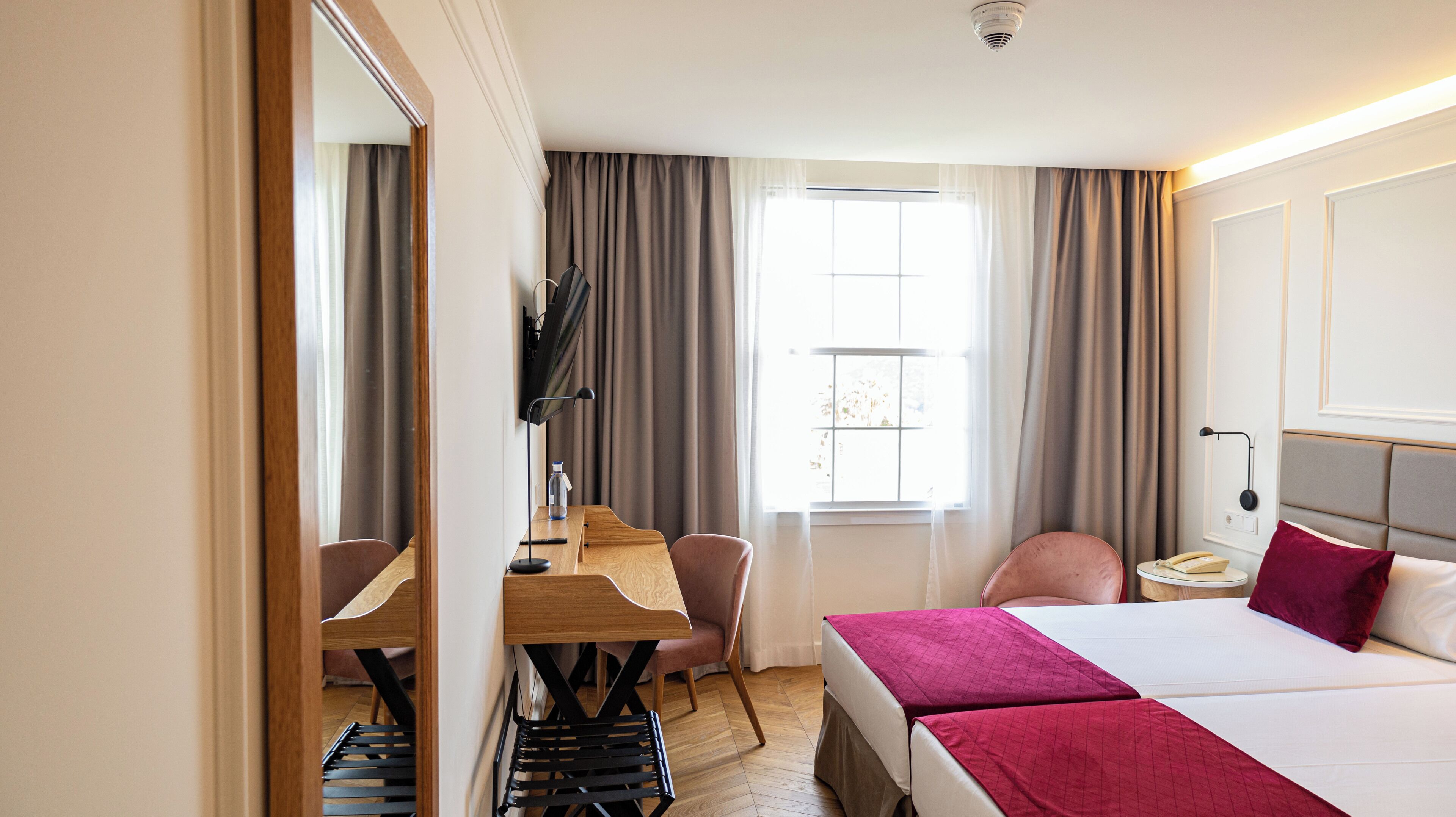 A hotel room with a bed, desk, chair, and a window with curtains.