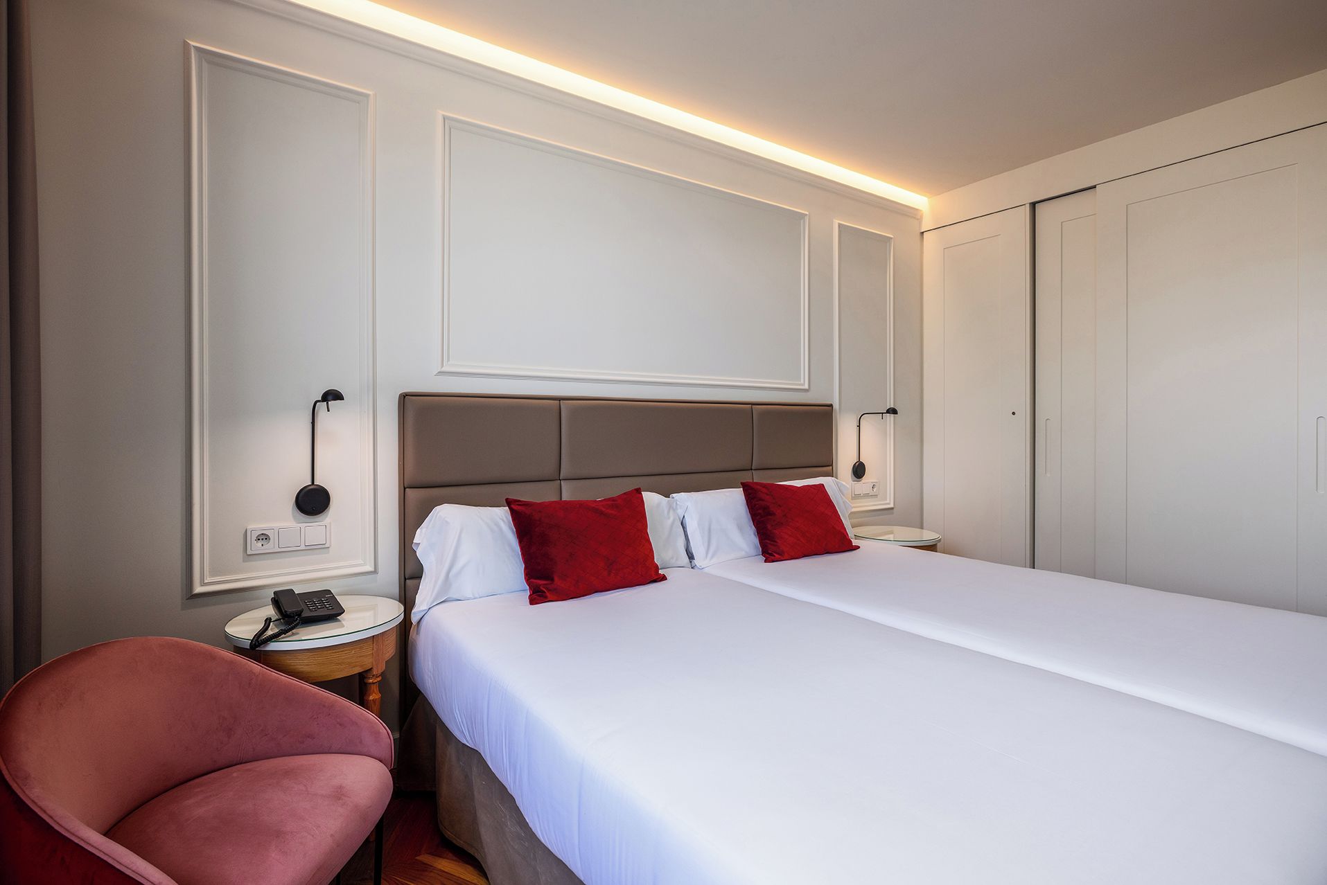 A hotel room with a bed, a chair, bedside tables, and a wardrobe.