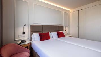 A hotel room with a bed, a chair, bedside tables, and a wardrobe.