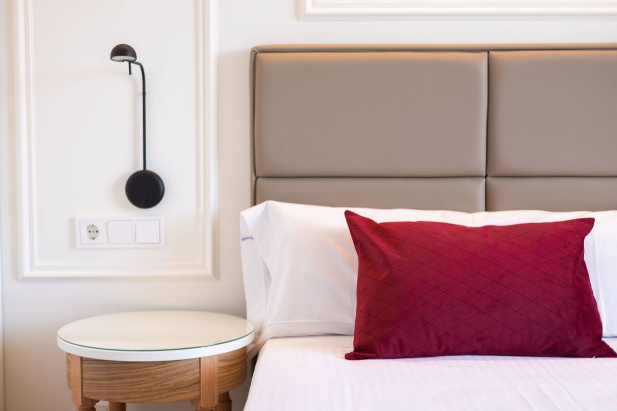 A neatly arranged bedroom with a bed, a bedside table, and a wall-mounted lamp.