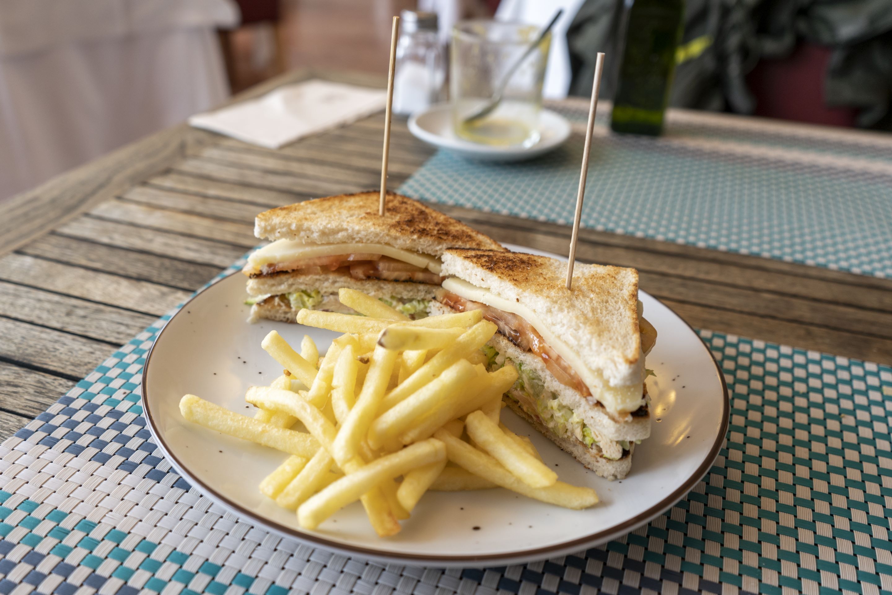 A plate with a sandwich and fries on a checkered tablecloth.