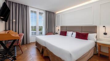 A hotel room with a large bed, a desk, a chair, and a TV.