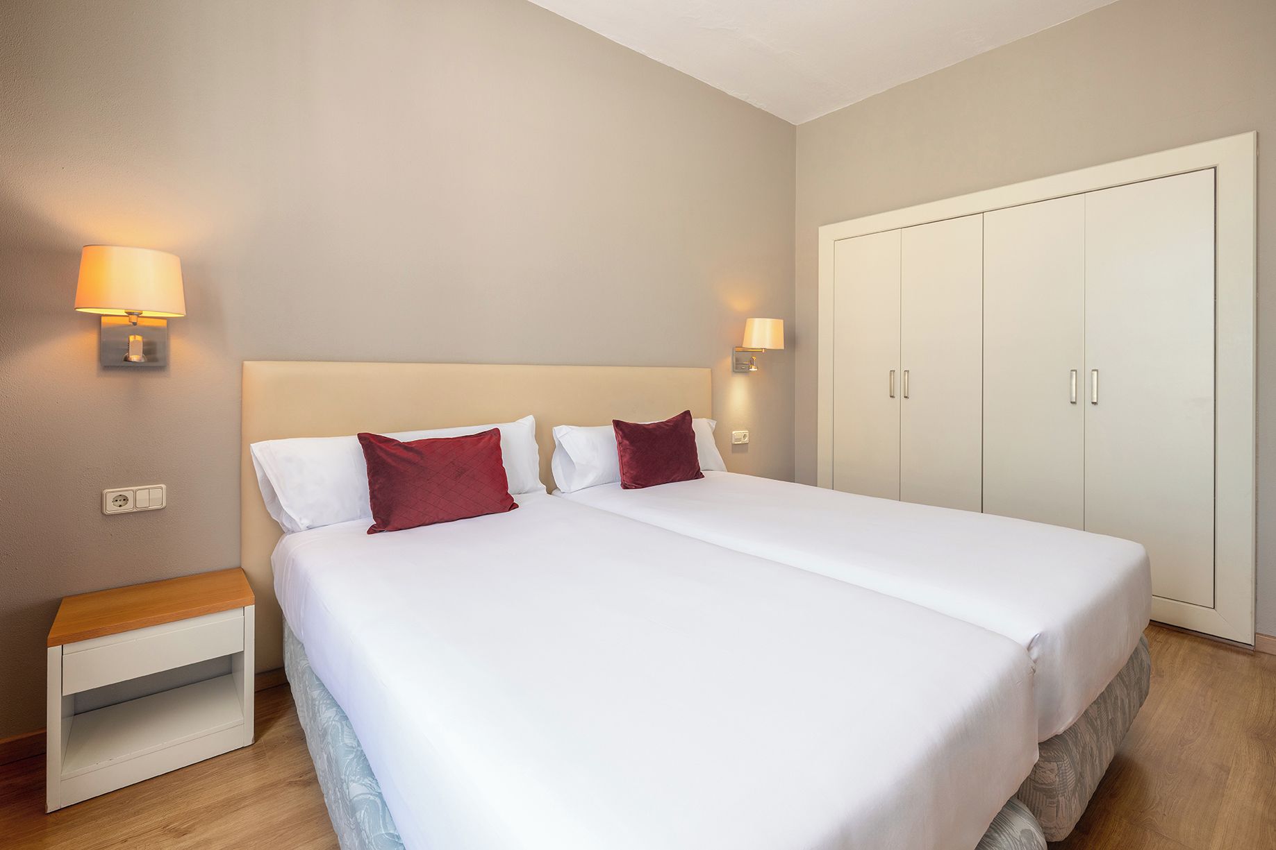 Una habitación de hotel con una cama grande, mesitas de noche, un armario y lámparas de pared.
