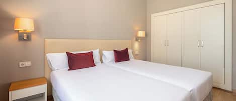Una habitación de hotel con una cama grande, mesitas de noche, un armario y lámparas de pared.
