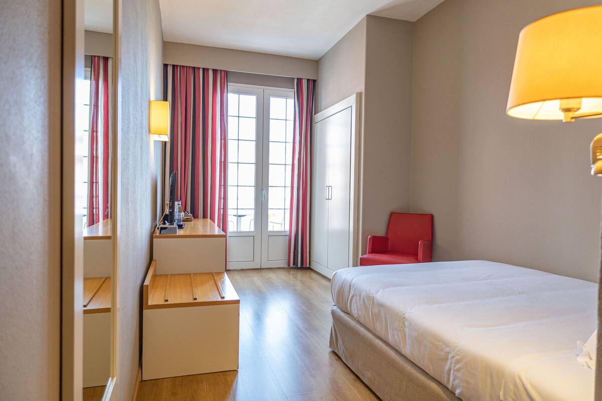 A hotel room with a bed, a desk, a chair, and a window with curtains.
