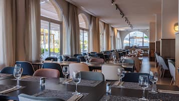 Um restaurante amplo com várias mesas e cadeiras, e grandes janelas que permitem entrada de luz natural.