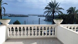 Un balcon avec vue sur la mer, des meubles en osier blancs et une balustrade blanche.