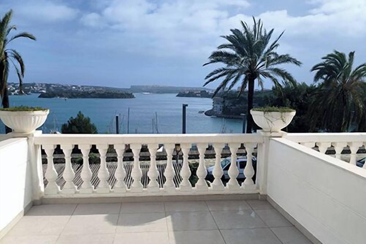A balcony with a view of the sea, white wicker furniture, and a white railing.