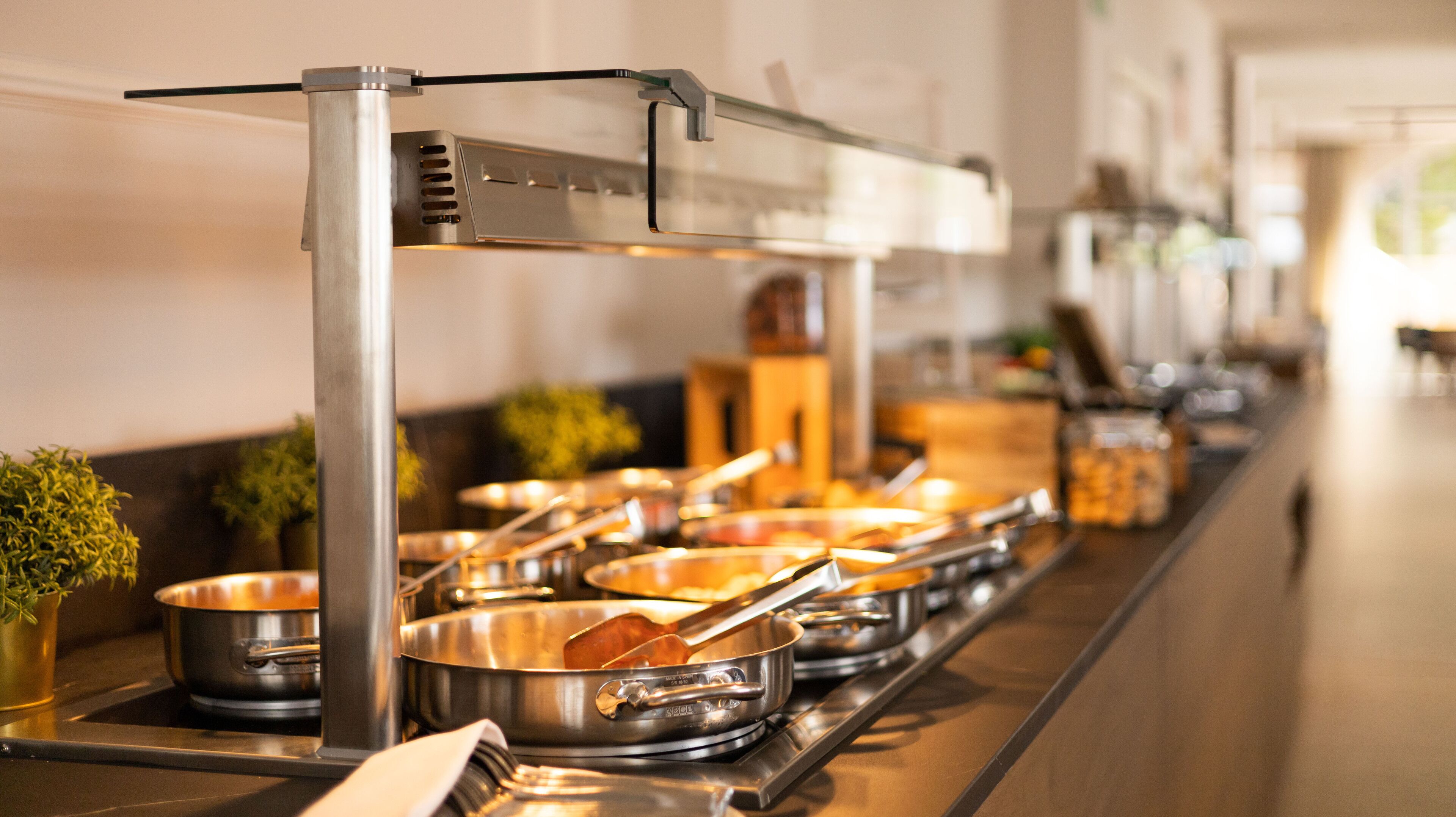 Un'attrezzatura per buffet con diverse postazioni di servizio in acciaio inox, ognuna con una pentola e una mestola.