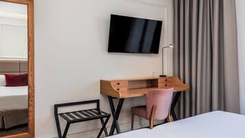 Habitación de hotel con cama, escritorio con silla, televisor montado en la pared y ventana con cortinas.