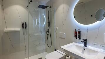 Un baño moderno con ducha envuelta en vidrio, un lavamanos blanco y un espejo redondo.