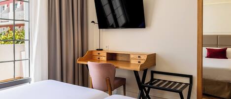 A hotel room with a bed, a desk with drawers, a chair, a TV mounted on the wall, and a large mirror.