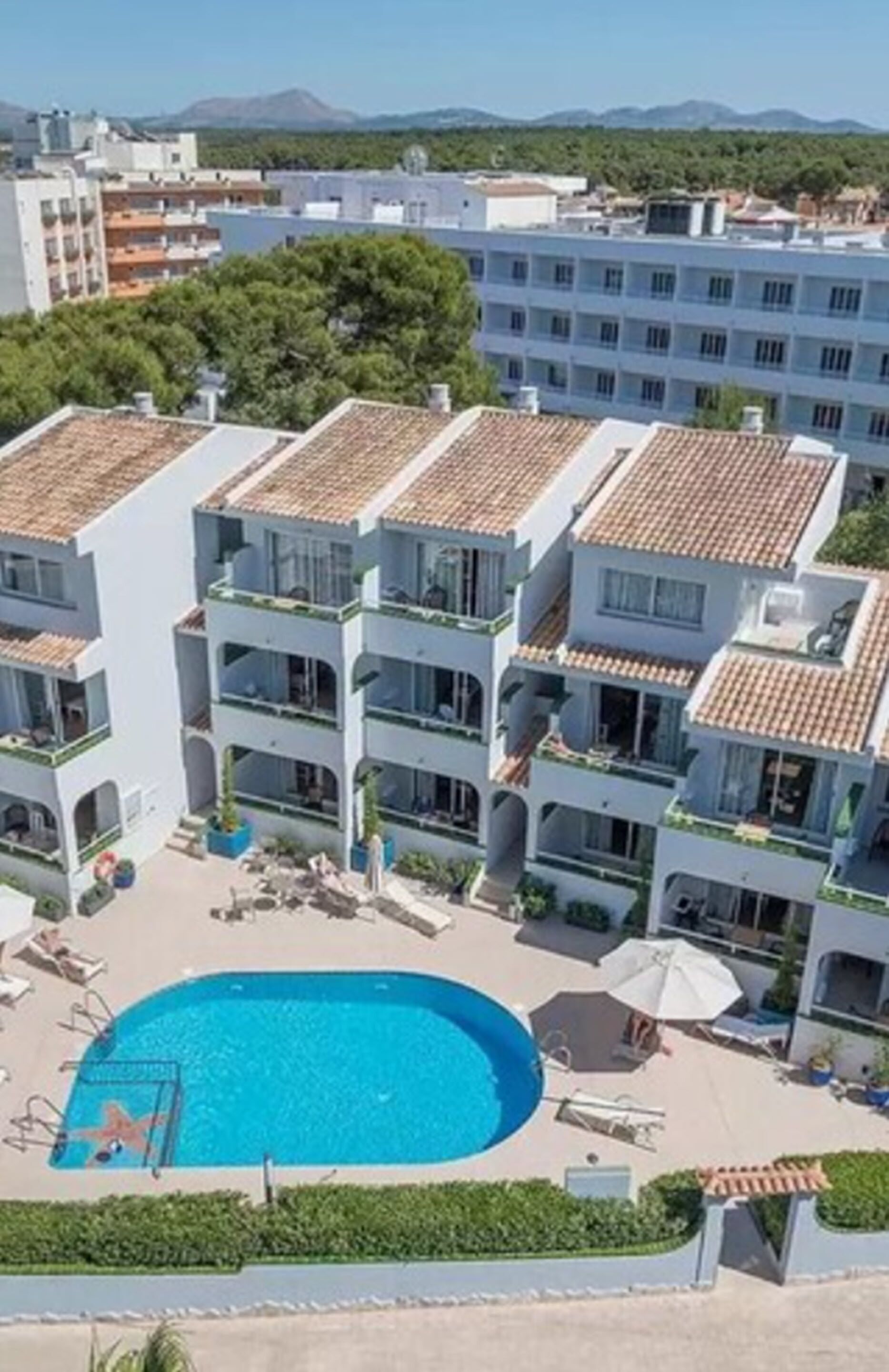A multi-story hotel with a swimming pool, outdoor seating, and a view of the surrounding area.