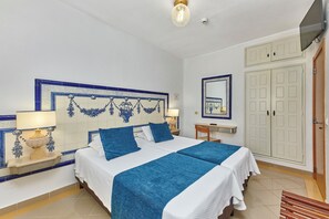 Ein Hotelzimmer mit einem Bett, zwei Nachttischen mit Lampen, einem Spiegel, einem Kleiderschrank und einem Fernseher.