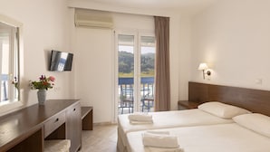 A hotel room with a bed, a desk, a TV, and a balcony with a view of the landscape. - Blue Sea (Samos)