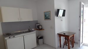 A compact kitchen with white cabinets, a sink, and a small table with a chair. - Blue Sea (Samos)