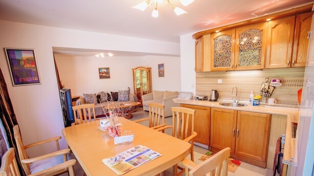 A dining area with a wooden table and chairs, a kitchen with wooden cabinets, and a sofa in the background. - Yassen Mng Apartments (Nessebar)