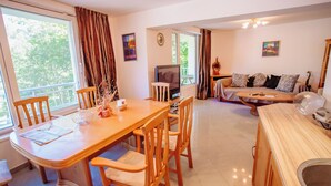 A dining area with a wooden table and chairs, a television, and a sofa with cushions. - Yassen Mng Apartments (Nessebar)