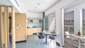 A modern kitchen with wooden cabinets, a dining area with a round table and chairs, and a balcony with a view of solar panels. - Anthea Hotel Apartments (Ayia Napa)