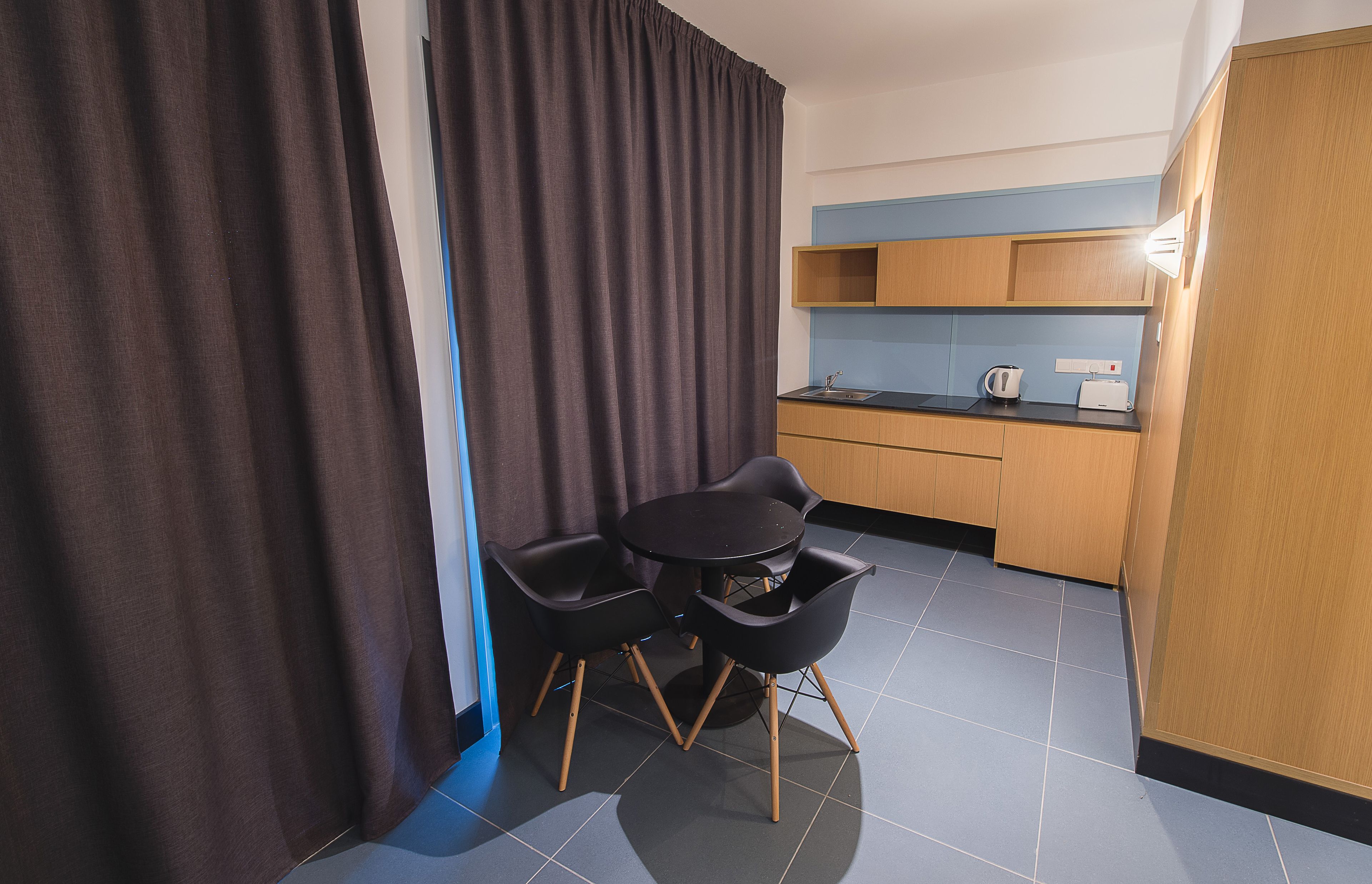A compact kitchen with a dining area, featuring a small table and chairs, a kettle, and a toaster.