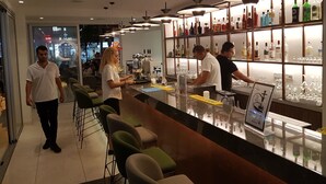 A bar area with a long counter, bar stools, and shelves stocked with bottles. - Anthea Hotel Apartments (Ayia Napa)