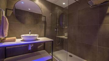 Un baño moderno con un espejo redondo, un lavamanos y una ducha con mampara de vidrio.