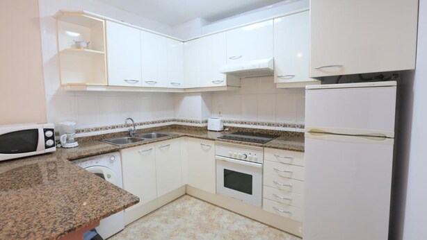 Cocina compacta con armarios blancos, microondas, tostadora, pileta y refrigerador.