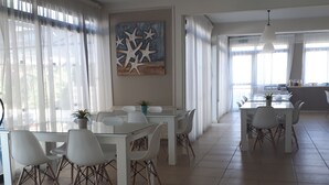 A spacious dining area with white tables and chairs, a large painting of starfish on the wall, and a view of the kitchen in the background. - Tasiana Star (Limassol)